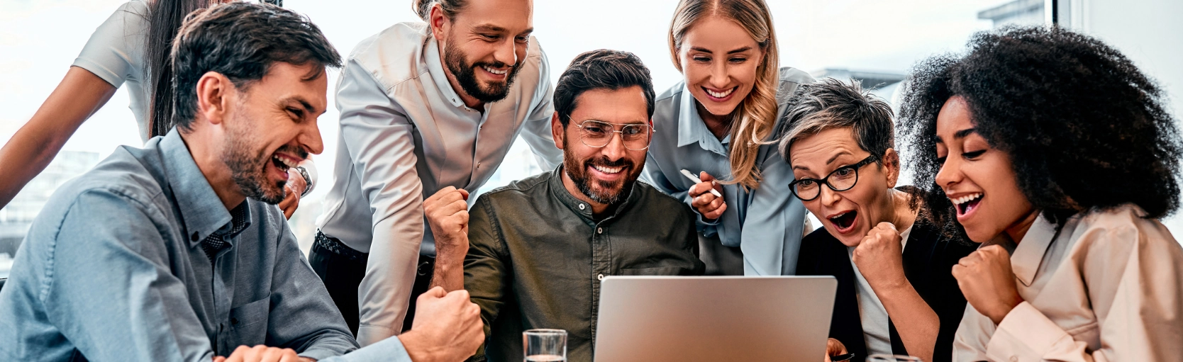 Diverse team collaborating around laptop celebrating success and teamwork in a positive work culture environment
